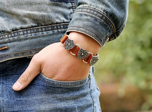 Close-up of vintage punk brown leather bracelet with embossed shield metal charms on wrist