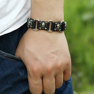Detail of punk leather bracelet featuring silver skull charms and metal link connectors