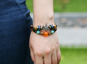 Primer plano de pulsera de cuero bohemia con dije de hoja de arce y cuentas