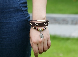 Detailed view of layered leather bracelet with beads and cowboy hat charm on wrist