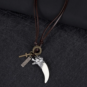 Détails de pendentifs dent de loup et croix en bronze sur un collier en cuir tressé marron