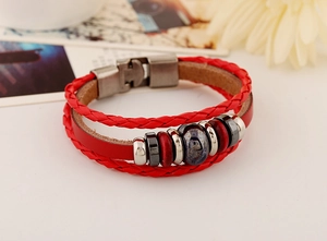 Dettaglio di un bracciale multistrato in pelle rossa con fibbia in metallo e perline decorative