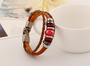 Detail of vintage multilayer braided leather bracelet with red ceramic bead and metal clasp