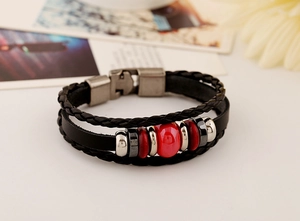 Detail of multi-layer black leather bracelet featuring a vibrant red ceramic bead and silver clasp