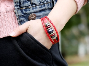 Dettaglio di un bracciale multistrato in pelle rossa con perle di ceramica sul polso