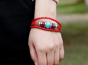 Detail of red multilayer leather bracelet with blue ceramic bead on a wrist outdoors