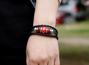 Detail of multilayer leather bracelet with red ceramic bead and punk metal accents