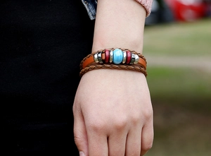 Detail of multi-layer leather bracelet with blue ceramic bead and brown woven cords