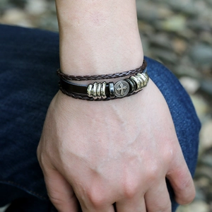 Close-up of layered leather bracelet with cross pendant on model in outdoor setting