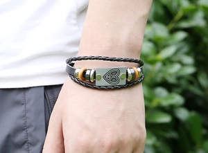 Detail of layered braided leather bracelet with heart peace sign metal plaque and beads