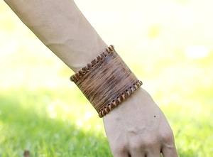 Close-up of vintage brown leather wide cuff bracelet with woven edge detail worn outdoors