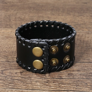 Detail of a wide black leather punk bracelet with bronze snaps on dark wood background