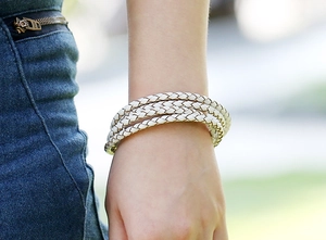 Detail of white multi-layer braided leather bracelet worn against denim fabric background