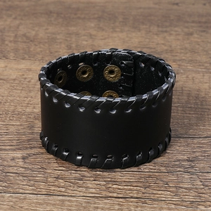 Detail view of black woven leather bracelet with adjustable gold snap buttons on wood