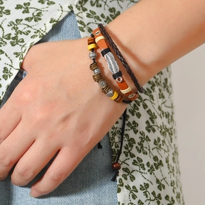 Close-up of multilayer leather bracelet with silver feather charm and wooden beads on wrist