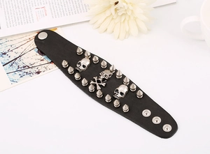 Detail of punk leather bracelet with metal skulls and rivets beside a white daisy