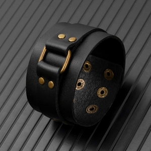 Close-up of punk leather bracelet with bronze buckles and studs on a textured surface