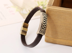Macro detail of bronze alloy plates with wave patterns on a brown leather bracelet