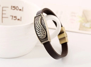 Detail of vintage brown leather bracelet with antique brass wing charm on a white mug