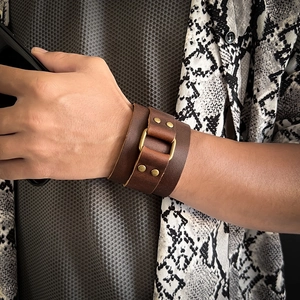 Macro view of wide brown cowhide leather wristband with vintage brass buckles and rivets