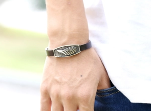 Detail of a punk leather bracelet with a vintage gold wing pendant worn on a wrist