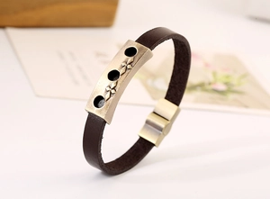 Detail of vintage brown leather bracelet featuring bronze cross plaque and magnetic clasp