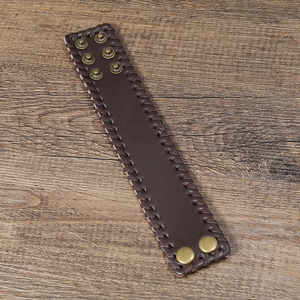 Retro wide dark brown leather cuff bracelet with woven edges on a wood background