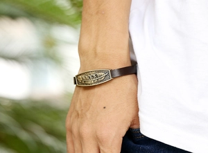 Close-up of vintage brown leather bracelet featuring a detailed golden metal feather charm