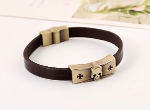 Detailed shot of punk skull and cross alloy plates on a brown leather braided bracelet