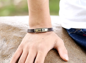 Detail of vintage dark brown leather bracelet with bronze cross charm on male wrist