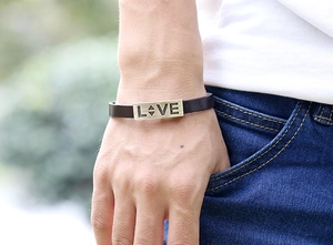 Macro detail of brown leather bracelet featuring an engraved LOVE metal plate on the wrist