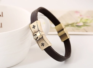 Detailed close-up of brown leather bracelet featuring bronze skull and iron cross motifs