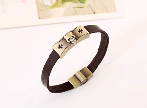 Detail of dark brown leather bracelet featuring a bronze skull and cross relief clasp