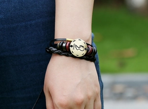 Gros plan du bracelet Gémeaux en cuir avec cordons tressés et breloque dorée gravée