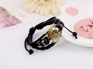 Macro shot of vintage bronze Pisces zodiac emblem on layered black braided leather bracelet