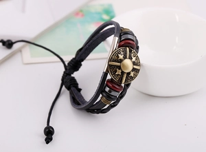 Detail of adjustable black leather bracelet with bronze shield charm and red wooden beads