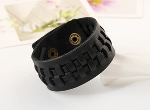 Dettaglio del bracciale in pelle nera intrecciata con bottoni a pressione in bronzo e trama