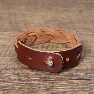 Detail of dark brown braided leather bracelet with adjustable metal buckle on wood