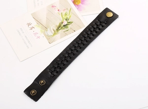 Dettaglio dell'ampio bracciale in pelle intrecciata nera con bottoni a pressione in bronzo