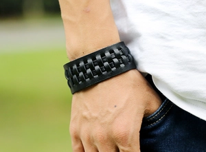 Dettaglio del bracciale largo in pelle nera intrecciata da uomo con trama artigianale