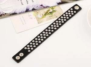 Détail d'un bracelet punk en cuir noir avec quatre rangées de rivets argentés et boutons pression