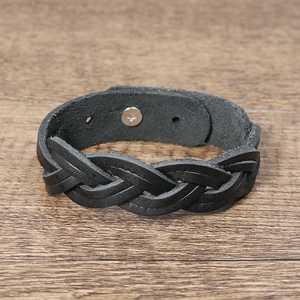 Macro detail of black braided leather bracelet featuring a silver metal snap fastener