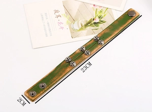 Detail view of vintage green leather punk bracelet with six metal skulls and snap buttons