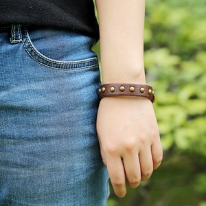 Punk style brown leather bracelet with metal rivets shown on wrist in outdoor setting