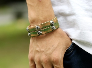 Detail of vintage green leather wrap bracelet with silver skull rivets on a model wrist
