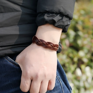 Close-up of a woven dark brown leather bracelet worn on wrist against a blurred nature background