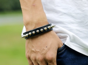 Detail of black leather punk bracelet with silver cone spikes shown on wrist outdoors