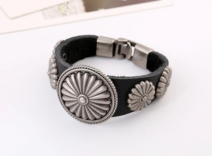 Détail macro du bracelet rétro en cuir noir avec disques métalliques floraux argentés
