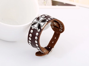 Detail of wide brown leather cuff bracelet featuring silver rivets and iron cross charm