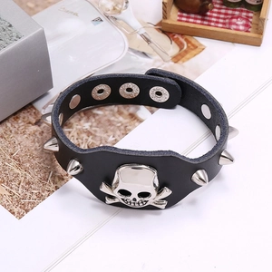 Punk black leather bracelet with silver skull charm and metallic studs on a wooden tray